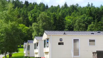 a row of houses with trees in the background at Moffat Manor Holiday Resort in Beattock