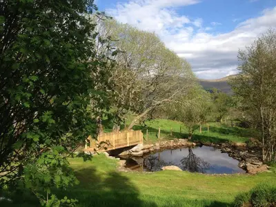 a bridge over a pond in a field at Wishing Well Cottage at Loch Tay and Hot Tub in Lawers