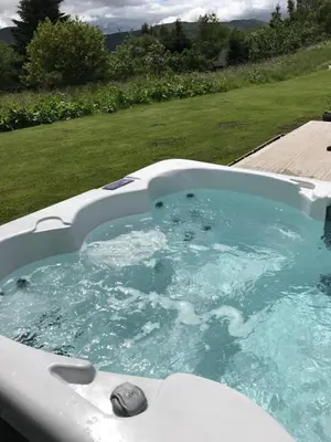 a bath tub filled with blue water in a yard at Sams Cottage with Loch Tay Vistas and Hot Tub in Lawers
