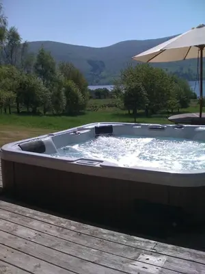 a large hot tub sitting on a deck with an umbrella at Ben Lawers Rest Cabin - Hot Tub and Loch Tay Vistas in Lawers