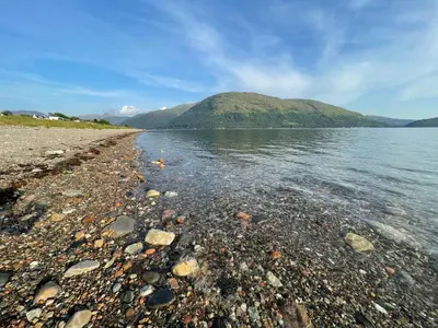 a rocky shore of a lake with a mountain in the background at Highland Nook in Fort William