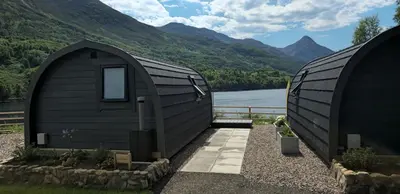two black domes with a view of a lake and mountains at Loch Leven Pods in Kinlochleven