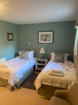 a bedroom with two beds and a chair at Fordie South Cottage in Comrie
