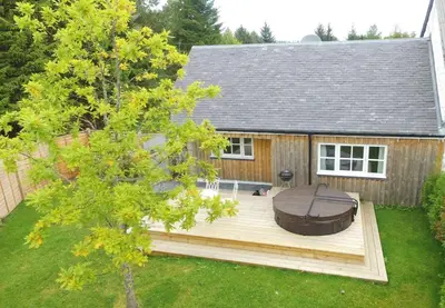 a backyard with a hot tub on a wooden deck at The Dairy Cottage, Loch Tay, Hot Tub and Garden in Lawers