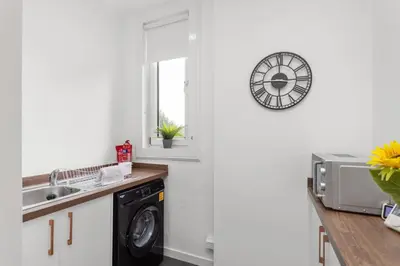 a kitchen with a washing machine and a clock on the wall at Stylish Stay in Inverkeithing. in Fife