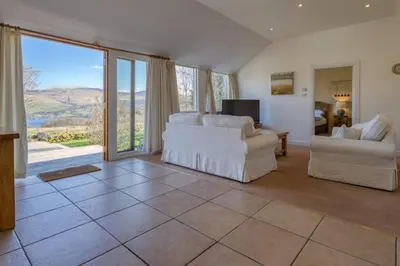 a living room with white furniture and large windows at Oak Cottage and Hot Tub, Loch Tay in Lawers