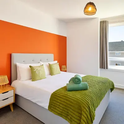 a bedroom with a large bed with an orange wall at Walk to Hydro and SEC Modern 3BR Free Parking in Glasgow