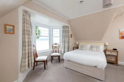 a bedroom with a bed and two chairs and a window at Camus House, Lochside Guest House in Onich