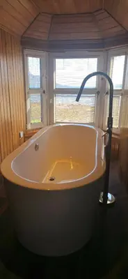 a large bath tub in a room with two windows at The Bay Rooms at Glenisle Hotel in Lamlash