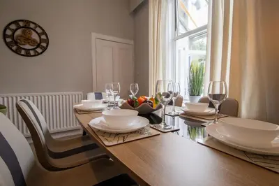 a wooden table with wine glasses and a bowl of fruit on it at Cairnhill House - cosy 3 bedroom in Airdrie