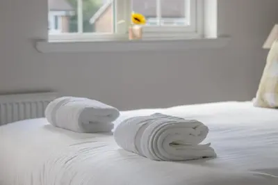a pile of towels on a bed with a window at Modern 2-Bedroom Home near Glasgow & Edinburgh in Airdrie