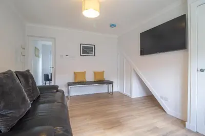 a living room with a black leather couch and a staircase at Modern 2-Bedroom Home near Glasgow & Edinburgh in Airdrie