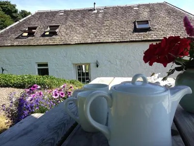 two cups sitting on a table in front of a house at Buzzard Cottage nestled in a hillside farm in Stirling