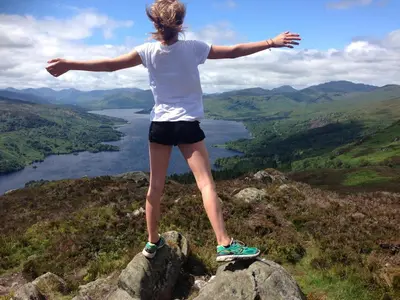 a woman standing on a rock with her arms outstretched at Buzzard Cottage nestled in a hillside farm in Stirling