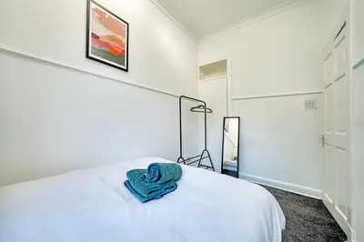 a bedroom with a white bed with a blue towel on it at 3BR Flat Near Maryhill Park and West End with Parking in Partick