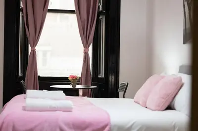 a bedroom with two beds with pink sheets and a window at Sauchihall Apartment in Glasgow