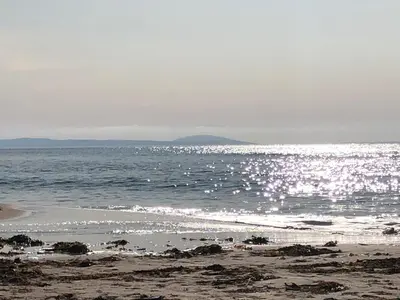 a beach with the sun reflecting on the water at Allt-Na-Craig Coach House - Ardrishaig in Ardrishaig