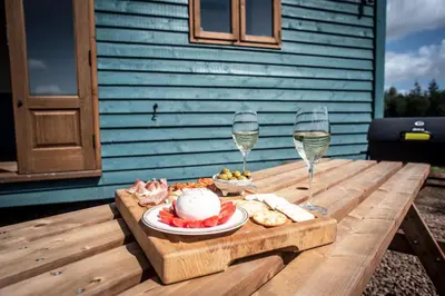 a table with a plate of food and two glasses of wine at Pentland Shepherd Huts in Penicuik
