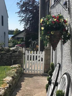 a white fence and a flower basket on a house at Oronsay, 2 Weint End Cottages, Great Urswick, Ulverston Cumbria LA120SP in Moffat