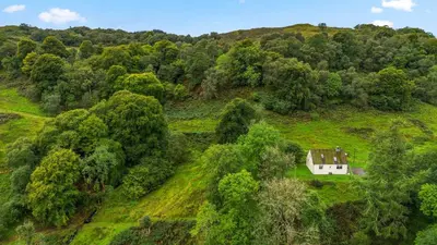 an aerial view of a house on a hill with trees at Charming 2-Bed Cottage on Tranquil Raera Farm in Kilninver