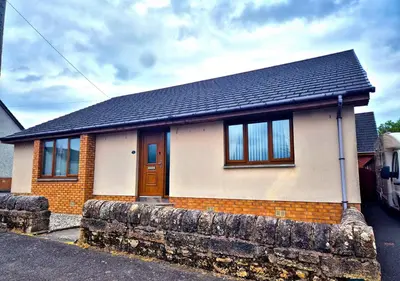 a small brick house with a black roof at The Yard Bungalow in Sanquhar