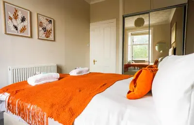 a bedroom with a bed with an orange blanket on it at Neilston Apartment in Paisley