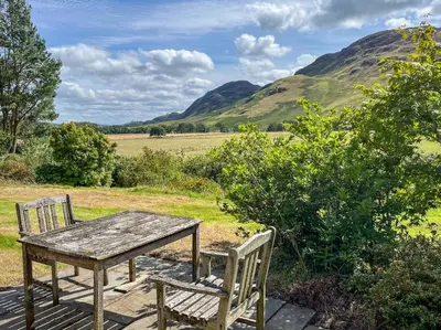 a wooden table and two chairs on a deck with mountains at 3 Bed in Comrie oc-e33307 in Comrie