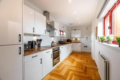 a kitchen with white cabinets and a wooden floor at Botanic House - 3BR Home - Private Parking in Glasgow