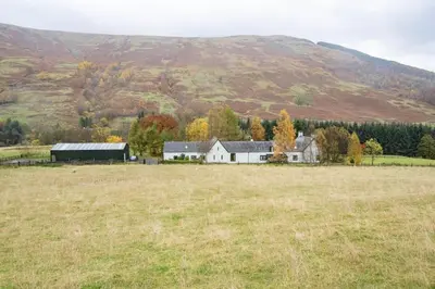a house in a field with a hill in the background at Glenogle Highland Estate Home in Lochearnhead