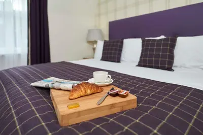 a tray with a croissant and a cup of coffee on a bed at Braid Apartments by Mansley in Edinburgh