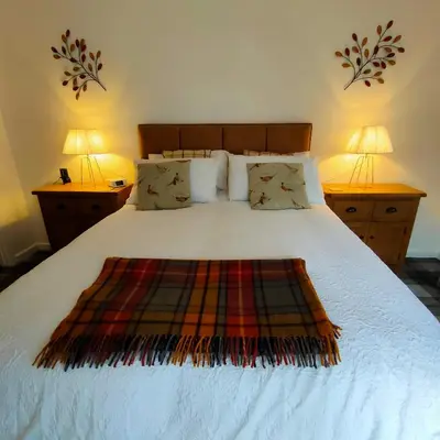 a bedroom with a large white bed with two lamps at The Old Smiddy Cottage and Apartment in Balloch
