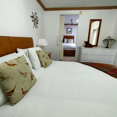 a bedroom with a large white bed and a mirror at The Old Smiddy Cottage and Apartment in Balloch