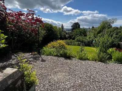 a garden with a gravel path and flowers and trees at Dungora House in Crieff