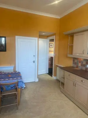 a room with a bed and a kitchen with yellow walls at Crawford House in Largs