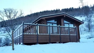 a log cabin in the snow with a railing at Sòghail Luxury Lodge and Balquhidder Mhor with Hot Tub in Kingshouse