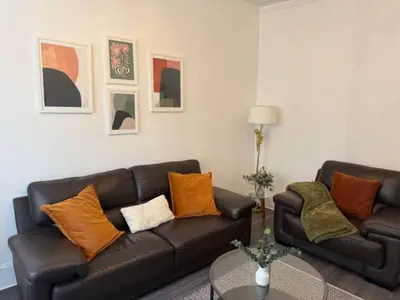 a living room with a black leather couch and orange pillows at 2BR Flat with Parking Near Glasgow Green and Parks in Glasgow