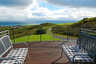 two benches sitting on a balcony looking at the ocean at Ocean View Lodge in Kilchiaran
