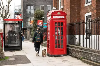a man walking a dog next to a red phone booth at 1 Bed Flat in Shoreditch near Station by Hostroo in Moffat
