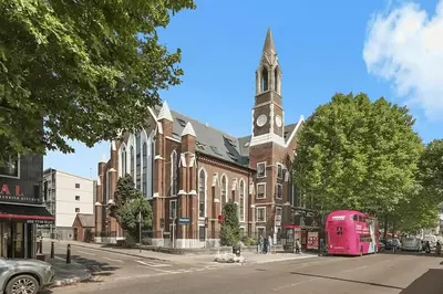 a pink bus parked in front of a brick building with a clock tower at 1 Bed Flat in Shoreditch near Station by Hostroo in Moffat