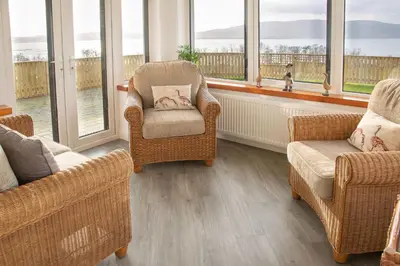 a living room with two chairs and a couch and windows at Sunset View in Innellan
