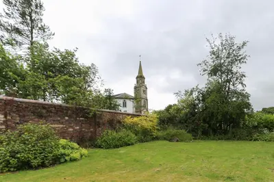 a building with a clock tower behind a brick wall at Fifty Five on Gilmour Street in Eaglesham