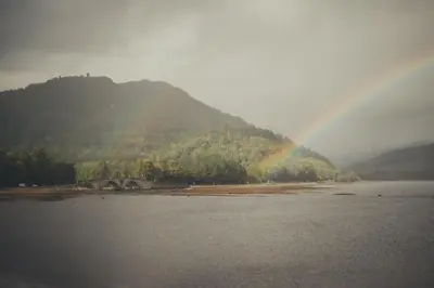 a rainbow over a body of water with a mountain at NICHT' Apartments Inveraray Town Centre in Inveraray