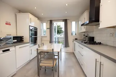 a kitchen with white cabinets and a table and chairs at Knightswood in Knightswood