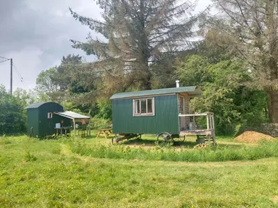 a green tiny house and a shed in a field at Shepherd's Hut Harmony at A Therapeutic Space in Moniaive