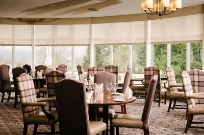 a dining room with tables and chairs and windows at Macdonald Forest Hills Resort in Aberfoyle