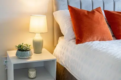 a bed with orange pillows and a lamp on a night stand at Modern 3 Bedroom home in Kings Park in Polmadie