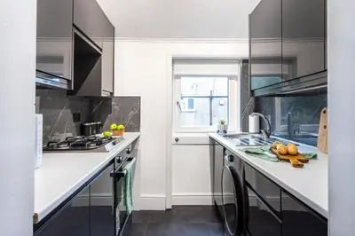 a kitchen with white counters and a sink and a window at Cosy 3 bed flat in Kings Park in Glasgow