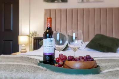 a bottle of wine and two wine glasses on a bed at Cosy 3 bed flat in Kings Park in Glasgow