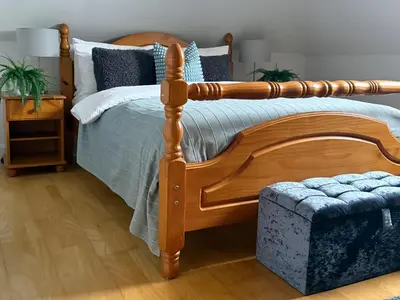 a bedroom with a wooden bed and a ottoman at Upstairs at Carlingford in Newton Mearns
