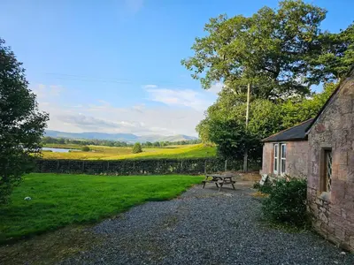a stone building with a picnic table next to a field at Morton Mains Cottage